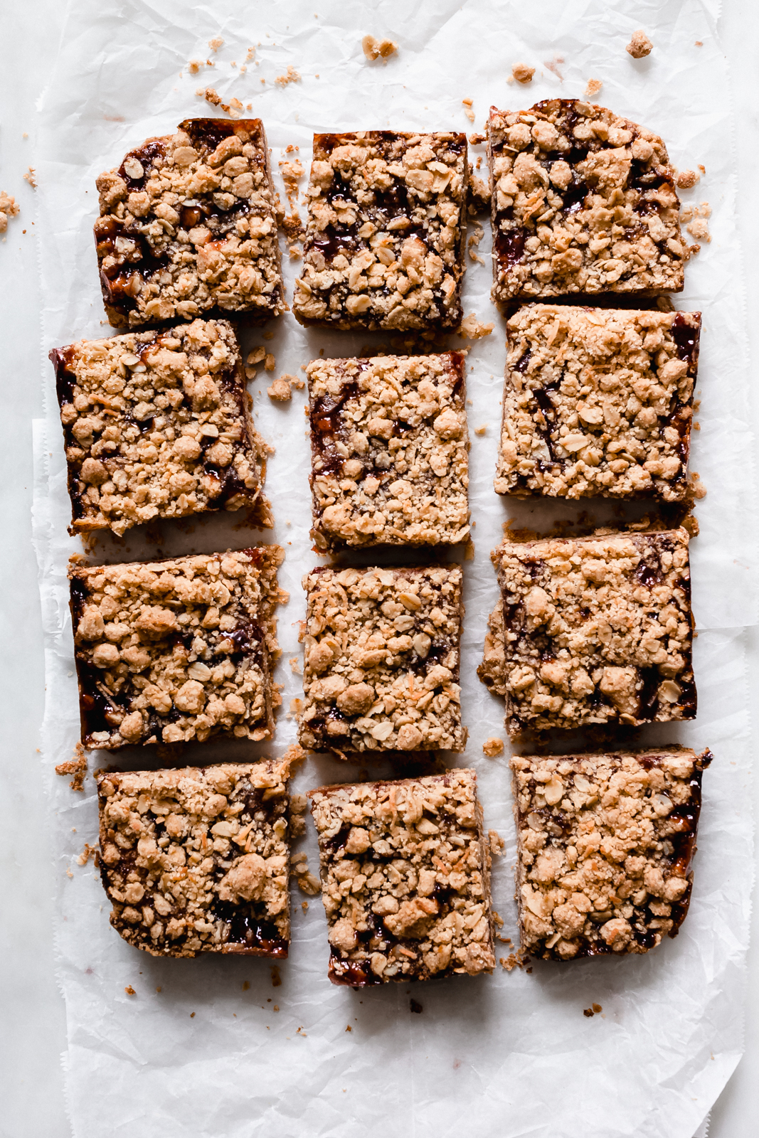 12 pieces of jelly oat bars on crumpled wax paper with scattered crumb topping