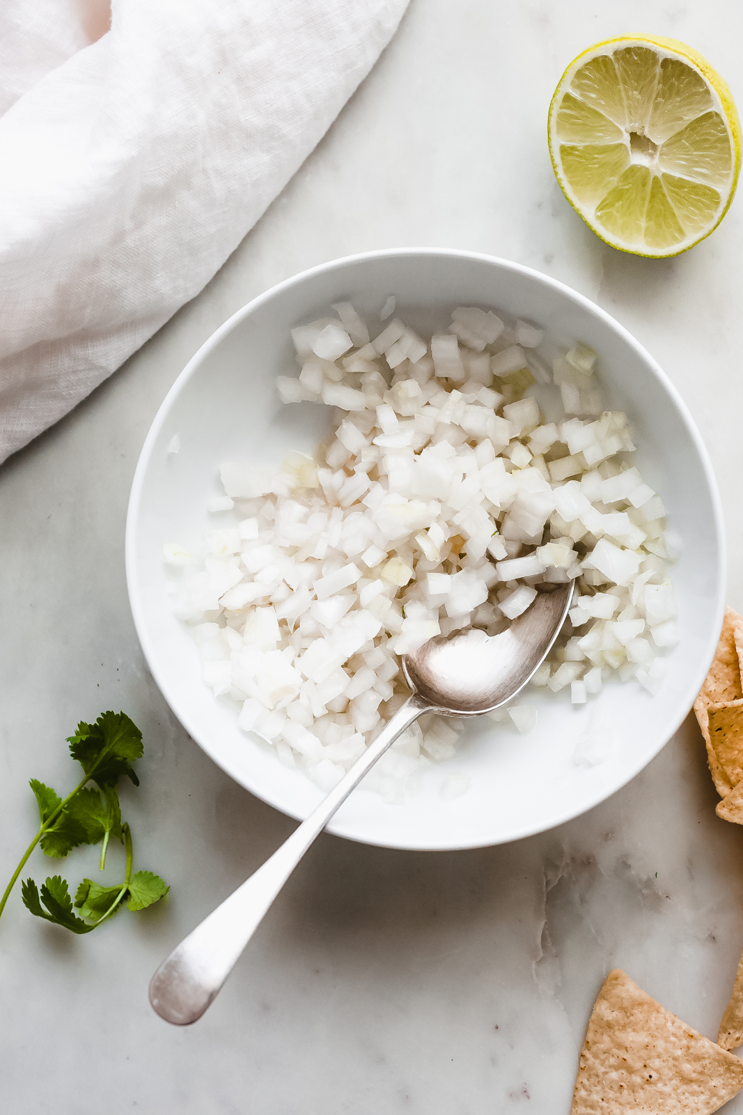 white bowl with chopped onions with metal spoon on white marble