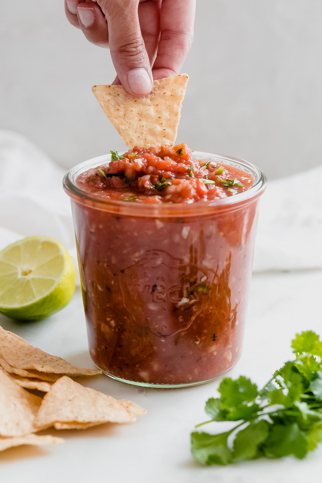 hand dipping tortilla chip into chunky salsa