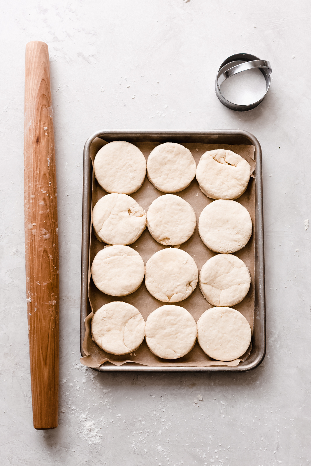 portioned buttermilk biscuit dough in sheet pan with rolling pin and cutter set next to pan