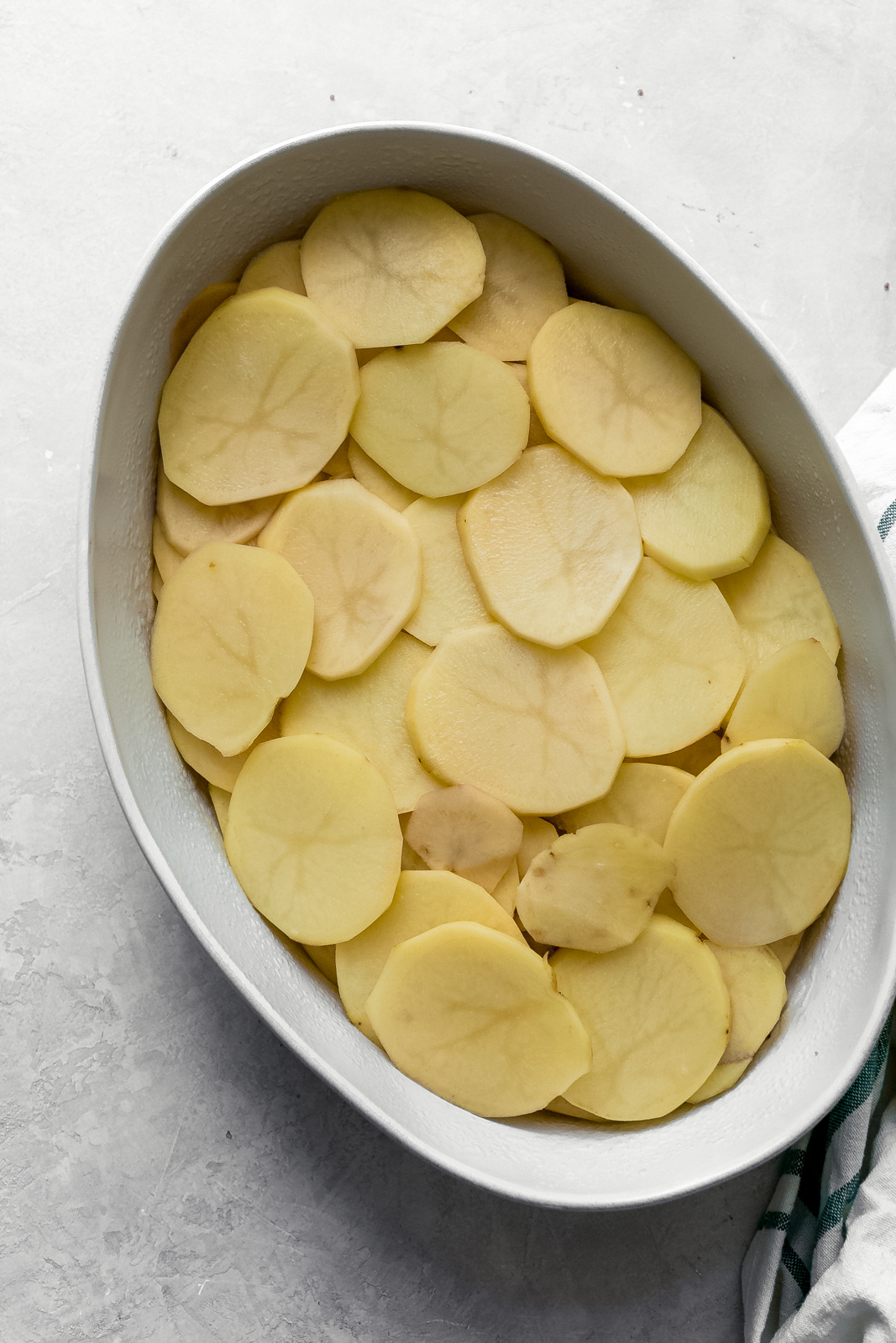 thinly sliced potatoes in oval baking dish on gray surface