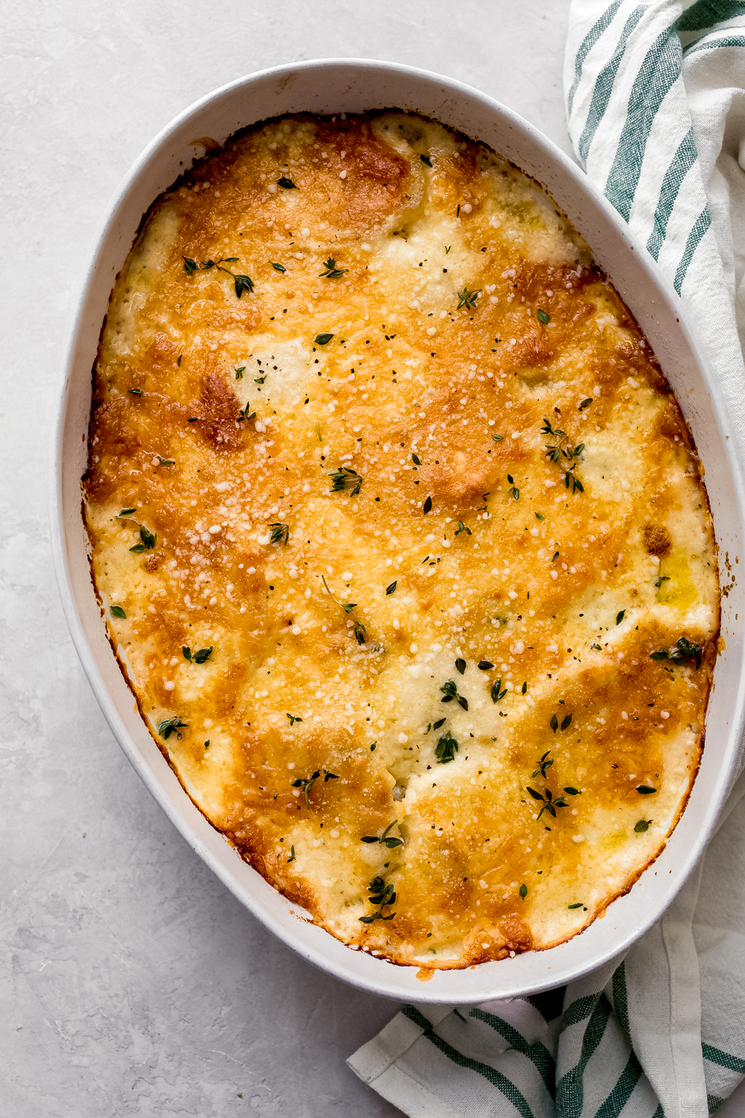 oval baking dish with scalloped potatoes topped with fresh thyme
