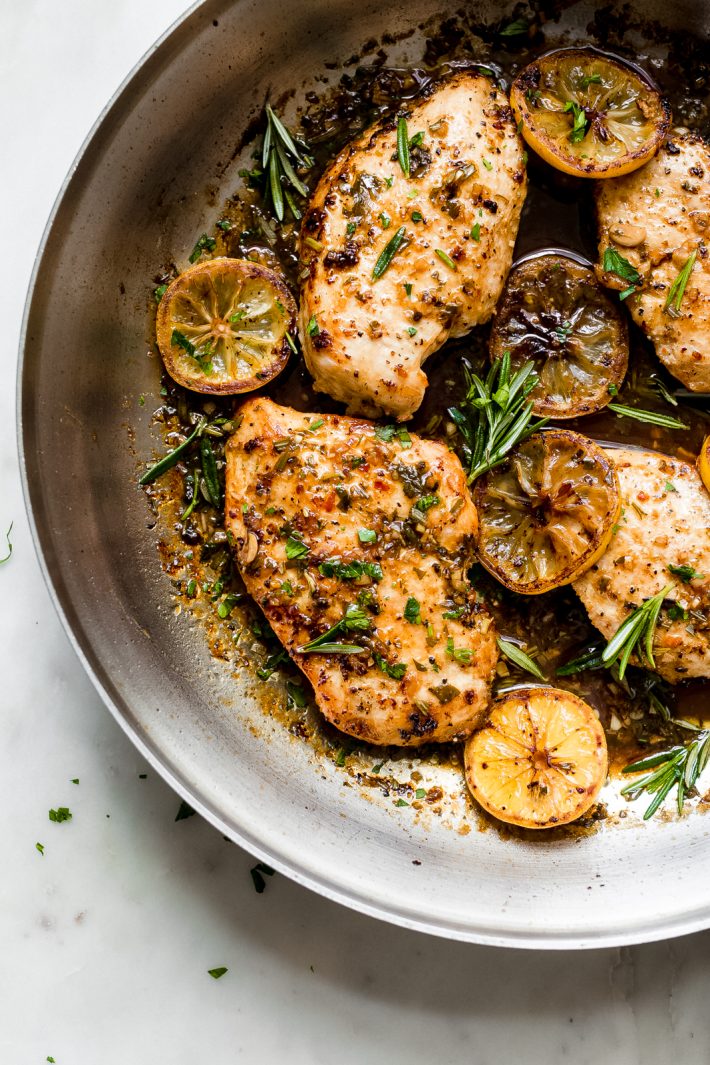 skillet with seared lemon rosemary chicken breasts with wilted lemon slices and fresh rosemary