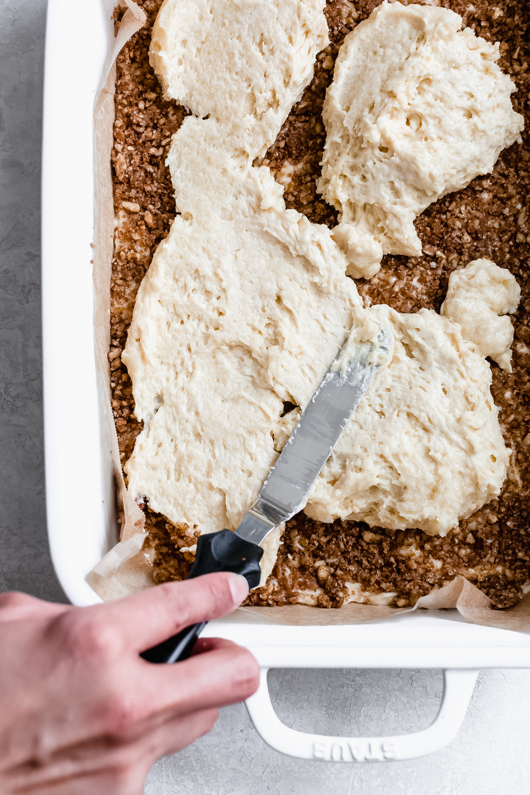 hand spreading top layer of coffee cake on sugar filling