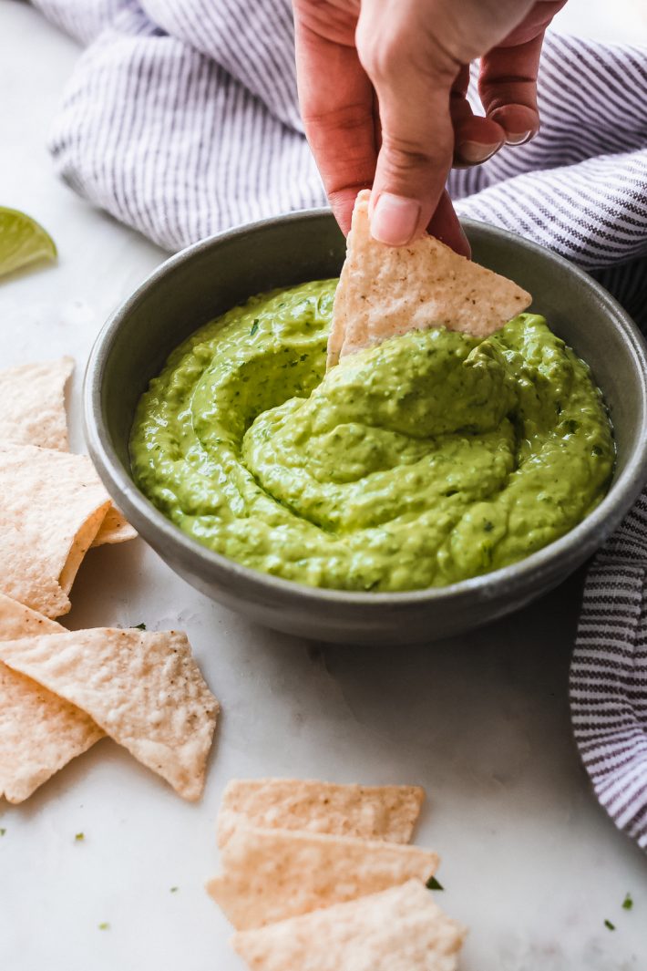 tortilla chip being dipped into blender avocado dip in olive colored bowl