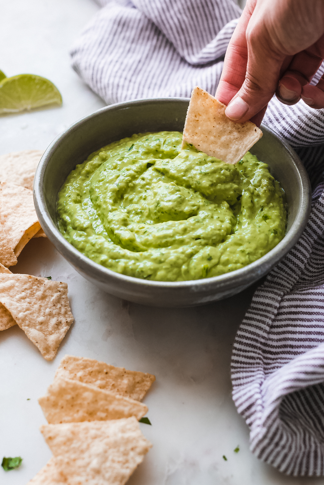 bowl of creamy avocado dip with hand dipping chip into bowl
