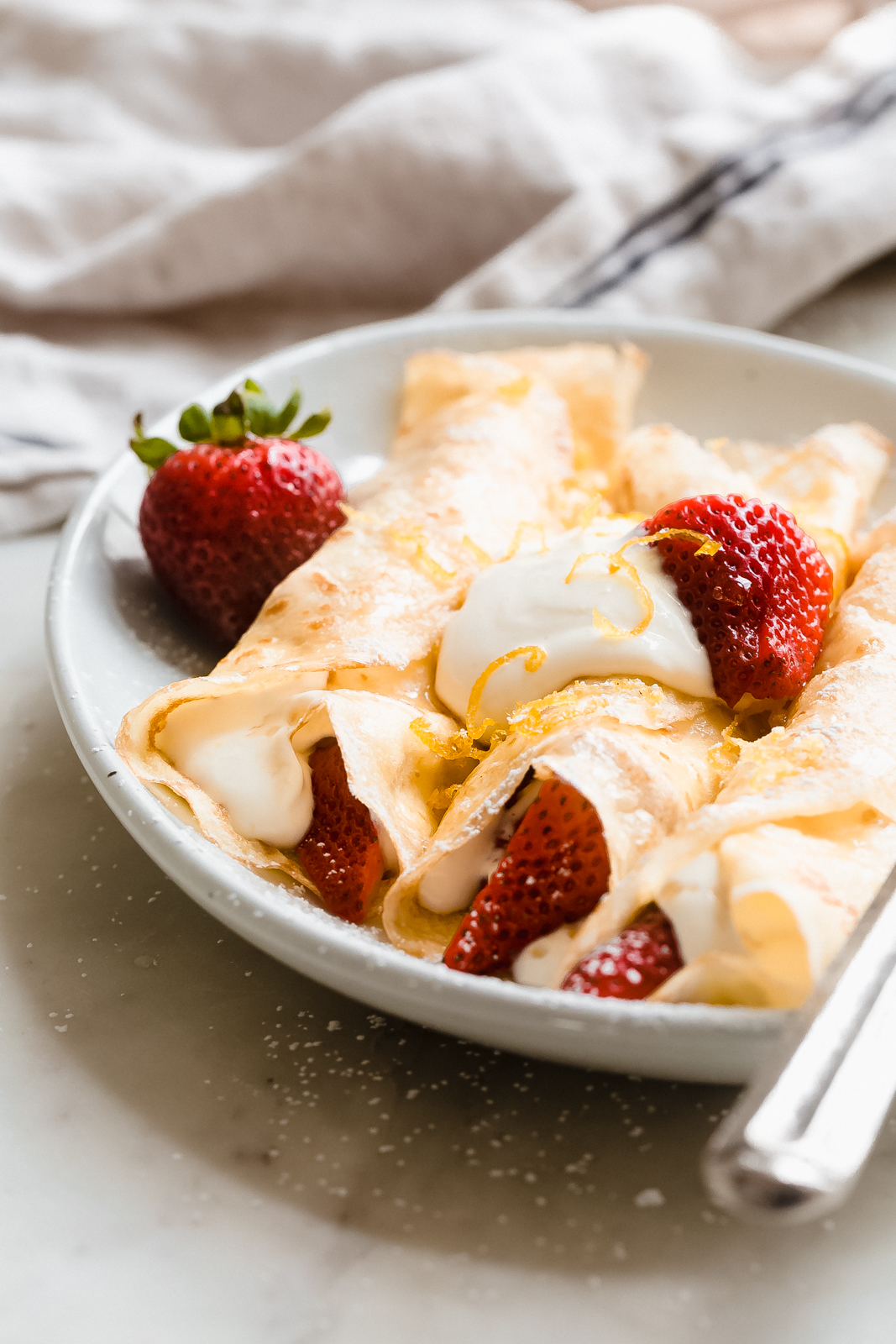 side shot of crepes stuffed with whipped cream and strawberries
