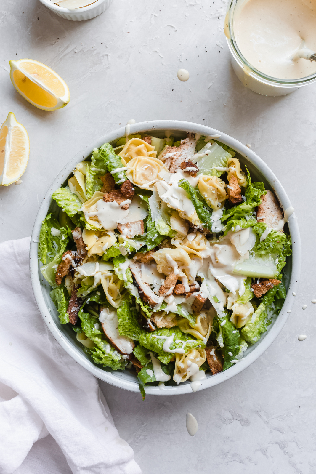 prepared tortellini Caesar salad in white speckled bowl on grey surface