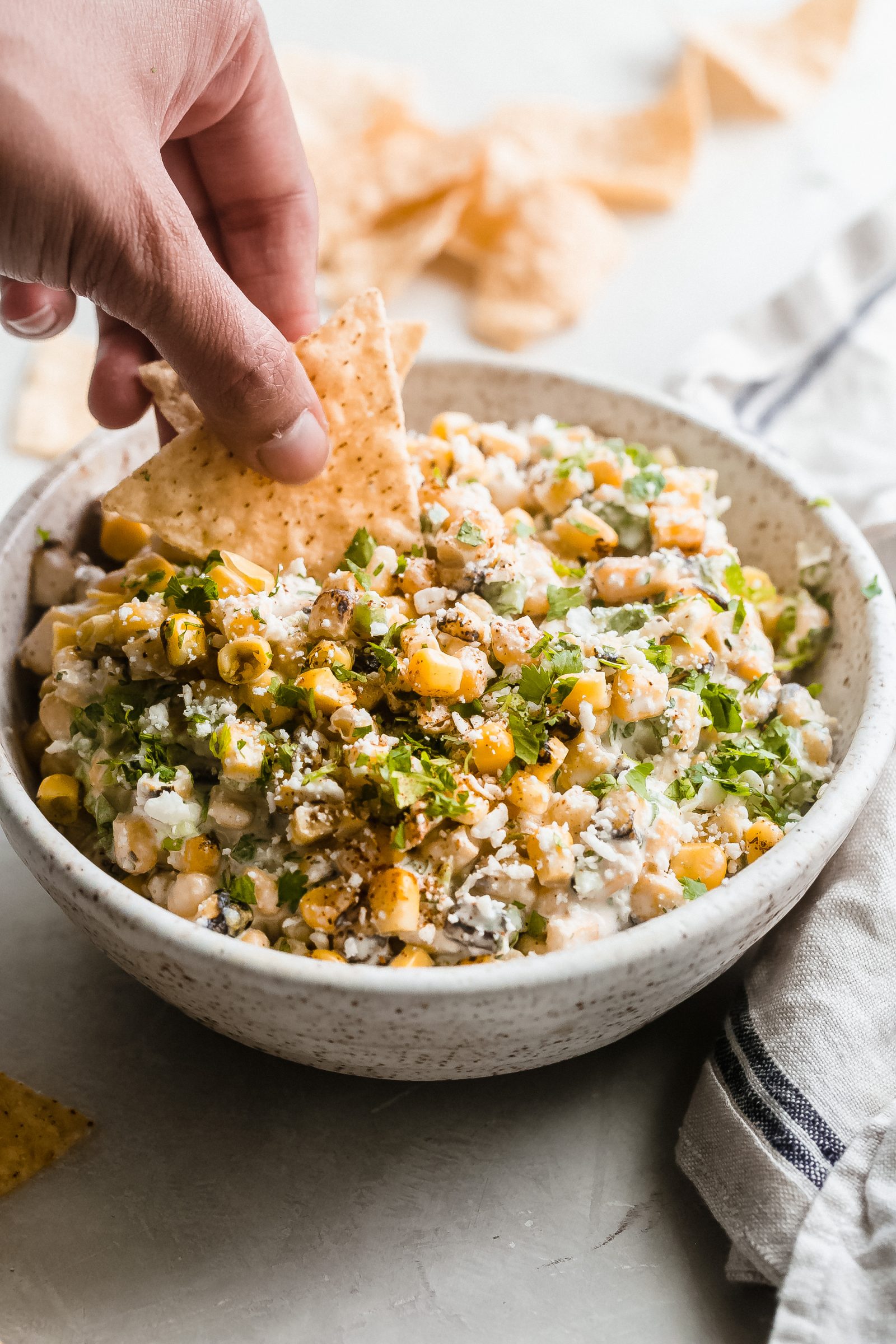 hand dipping corn tortillas in corn dip from bowl