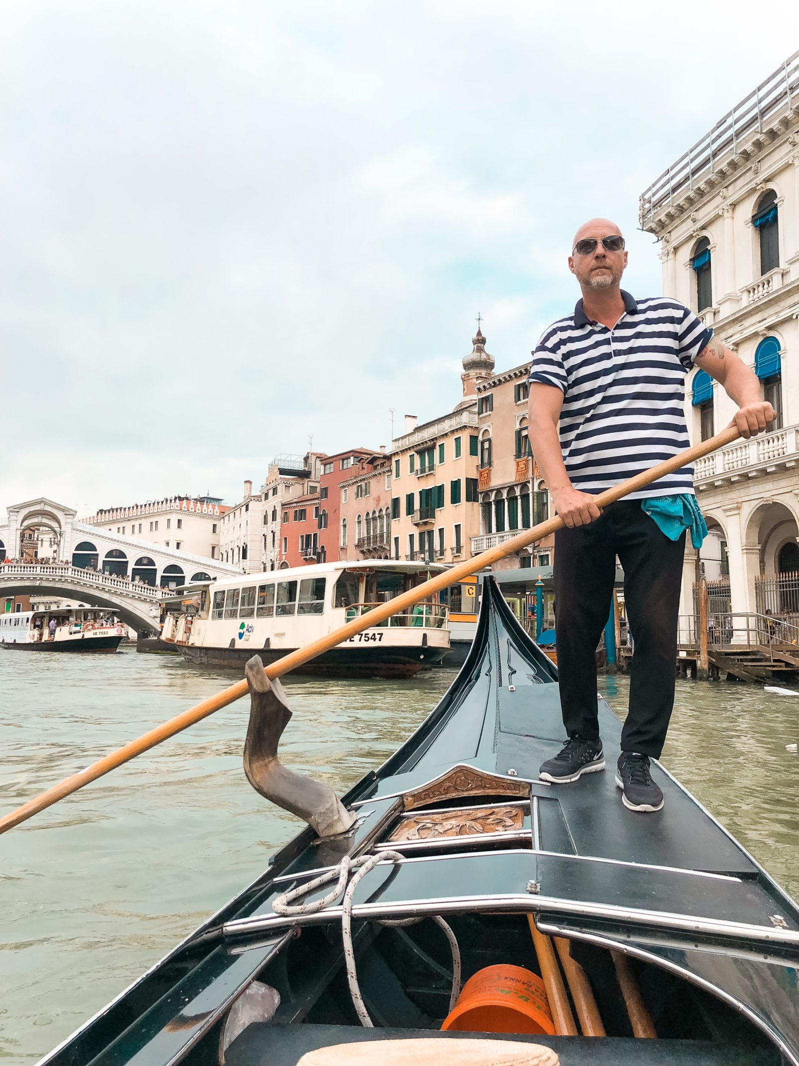 a picture of our gondolier with the Rialto bridge behind him