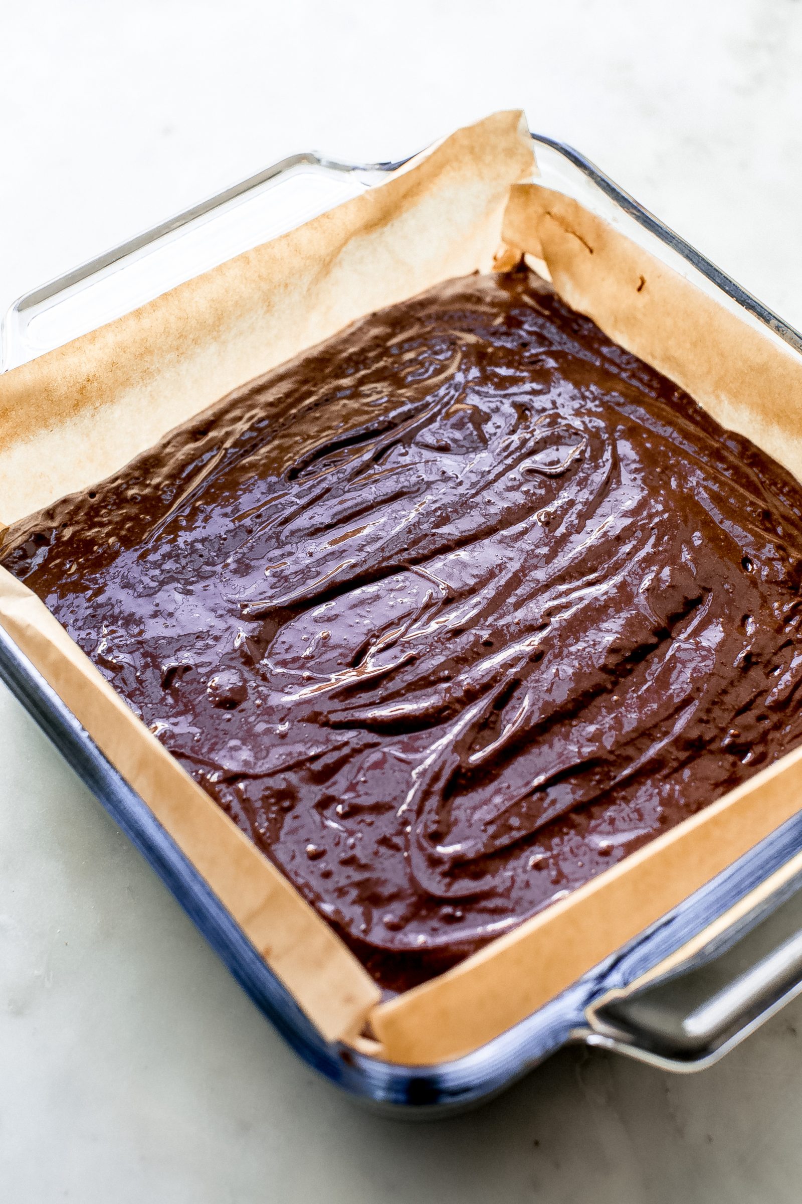 fudge brownie mixture spread in a glass baking dish lined with parchment paper