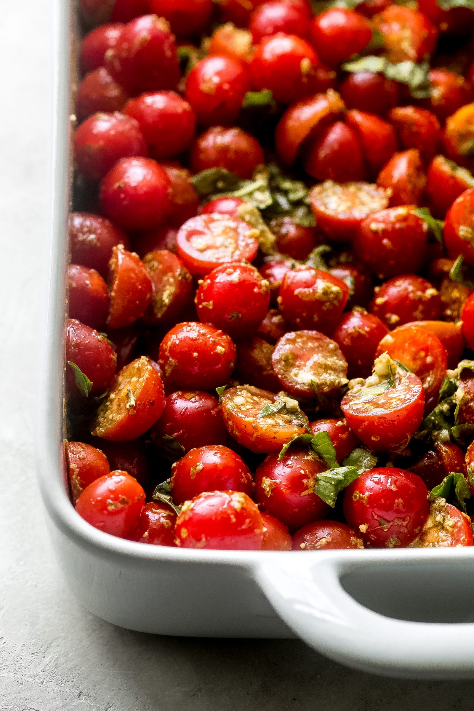 cherry tomatoes tossed with pesto and fresh basil in a baking dish