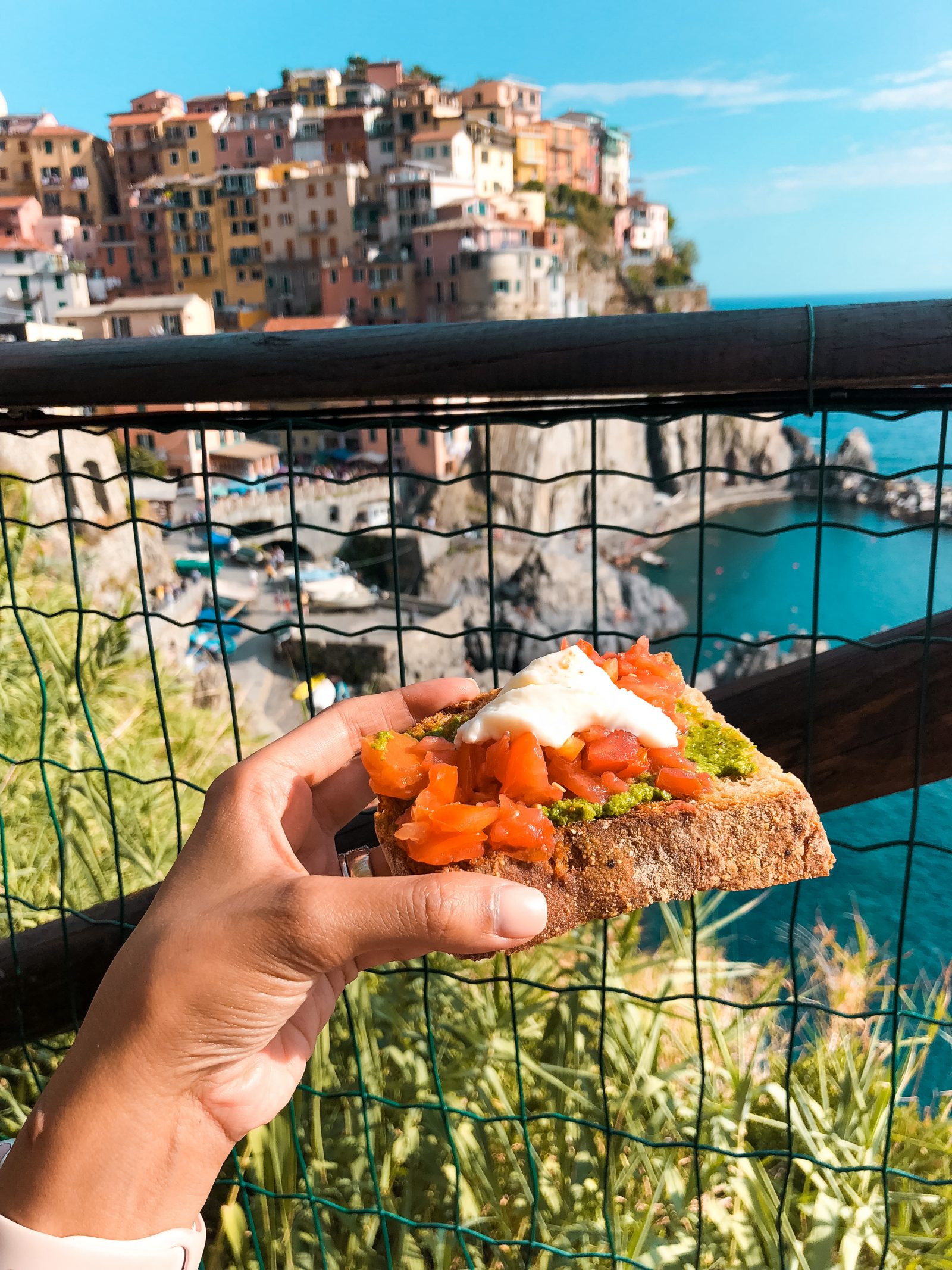 tomatoes, pesto, and ricotta on bread with Vernazza coastline in the backdrop