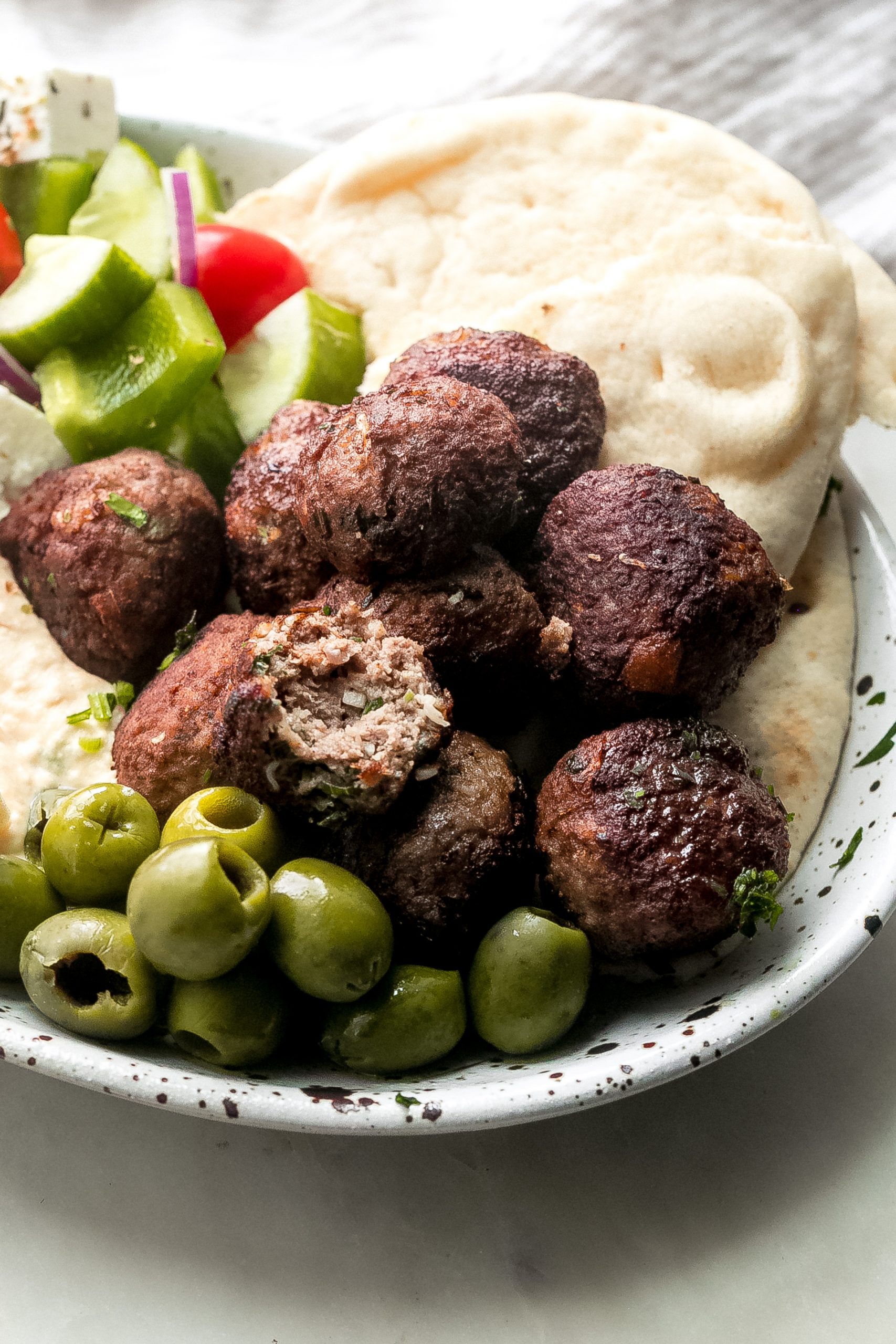 keftedes on a platter with pita, olives, salad, and hummus