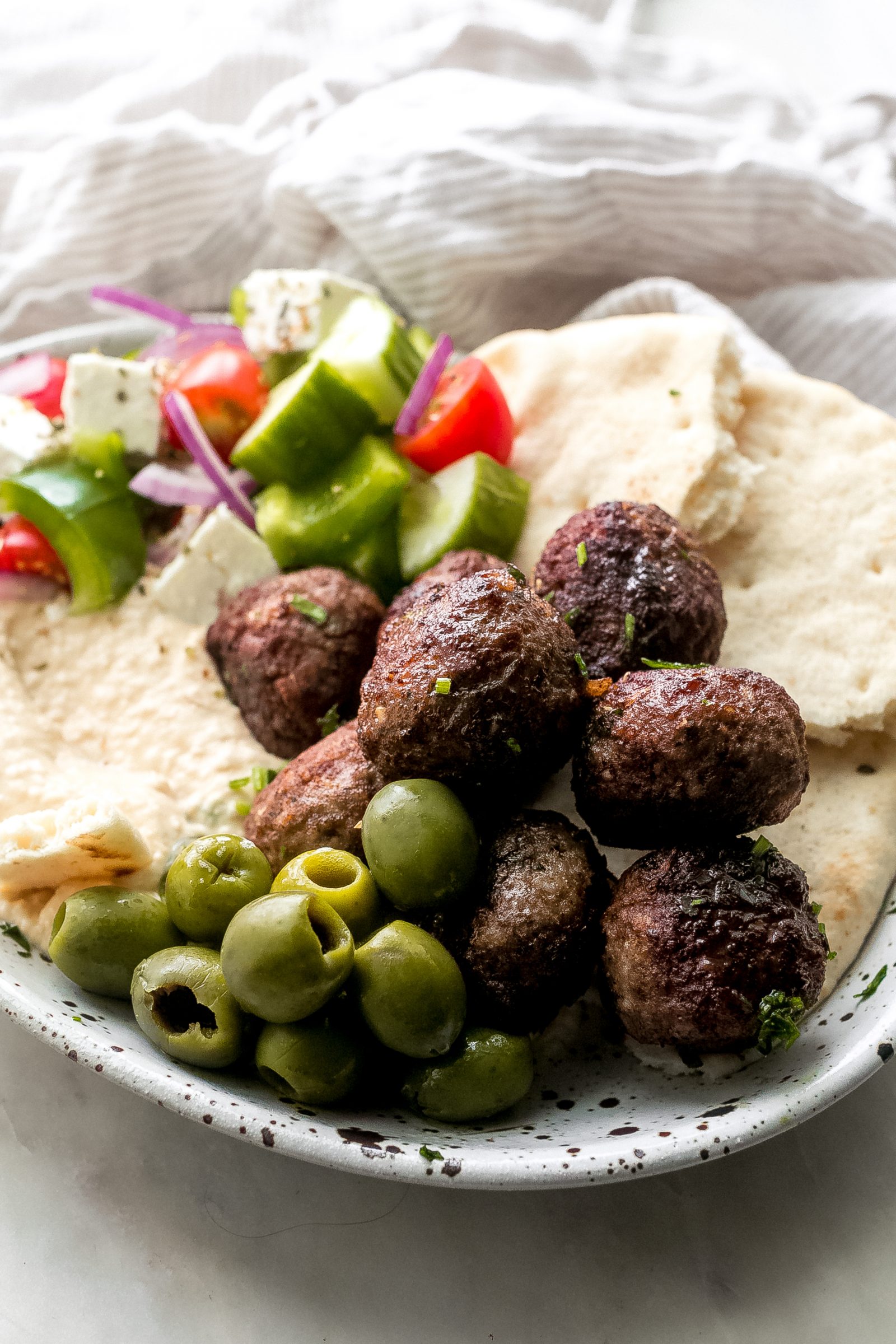 Greek Meatballs on speckled plate with hummus, bread, olives, and Greek Salad