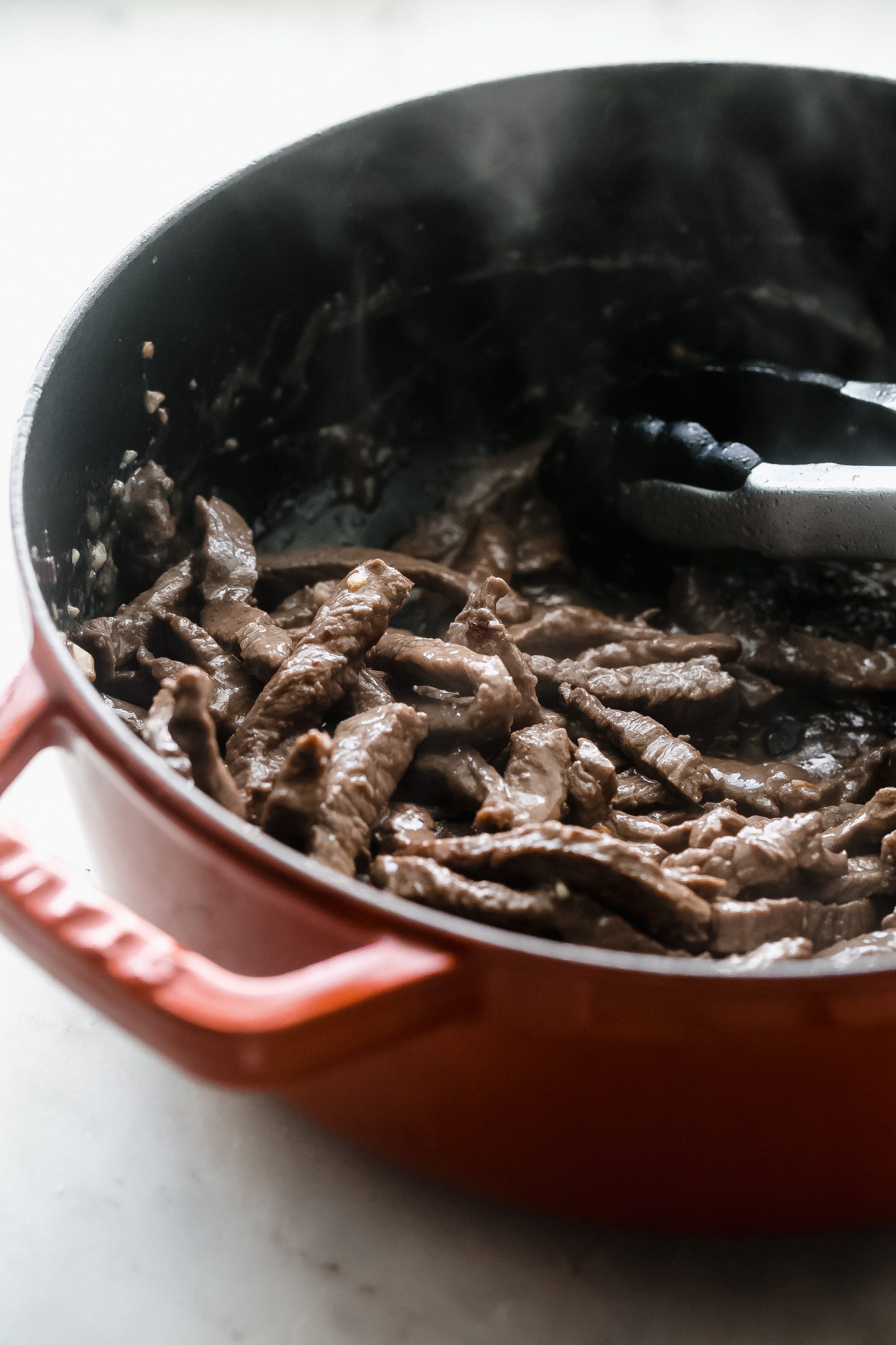 sautéed beef in cast iron pot with tongs