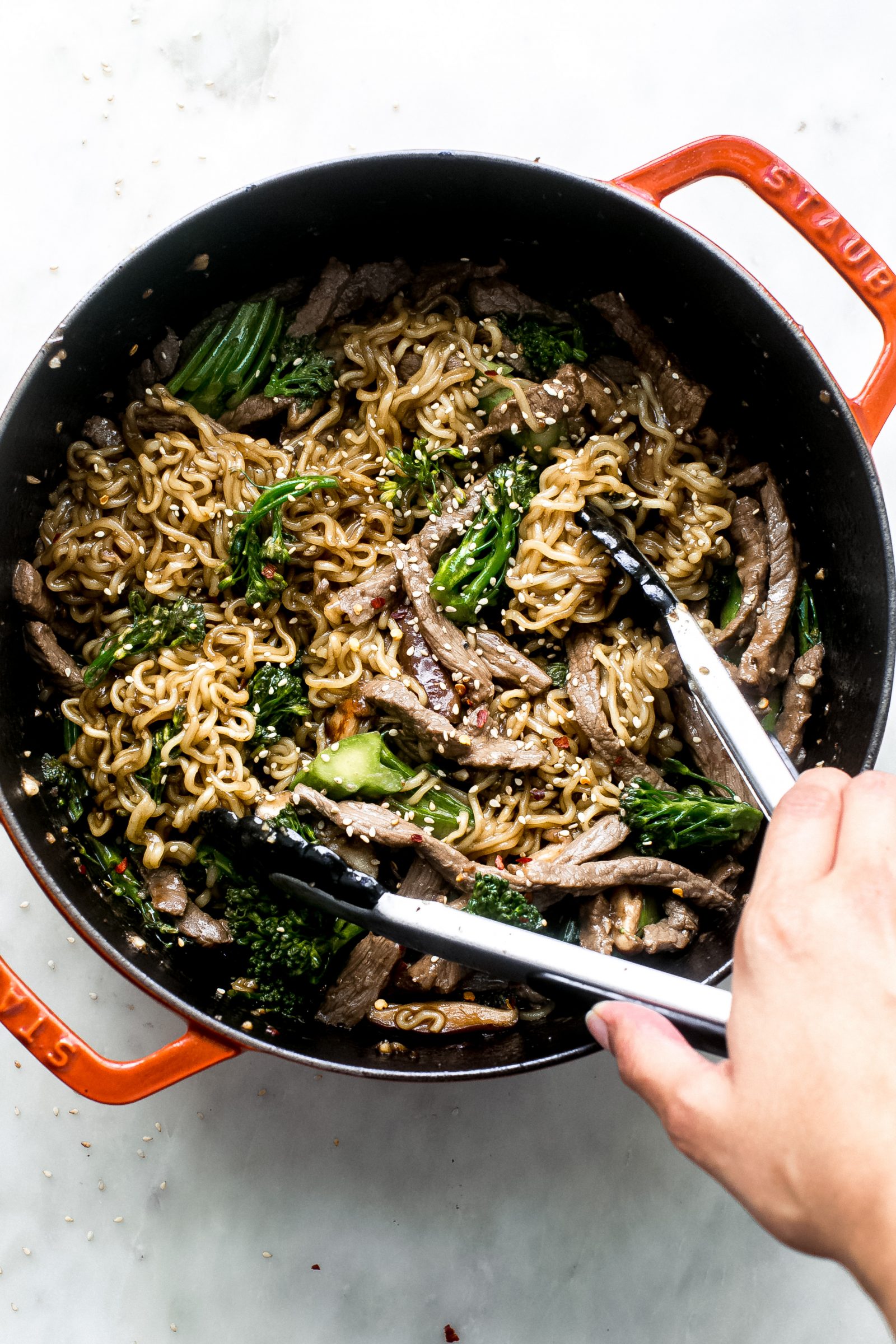 broccoli beef ramen being lifted with tongs from cast iron pot