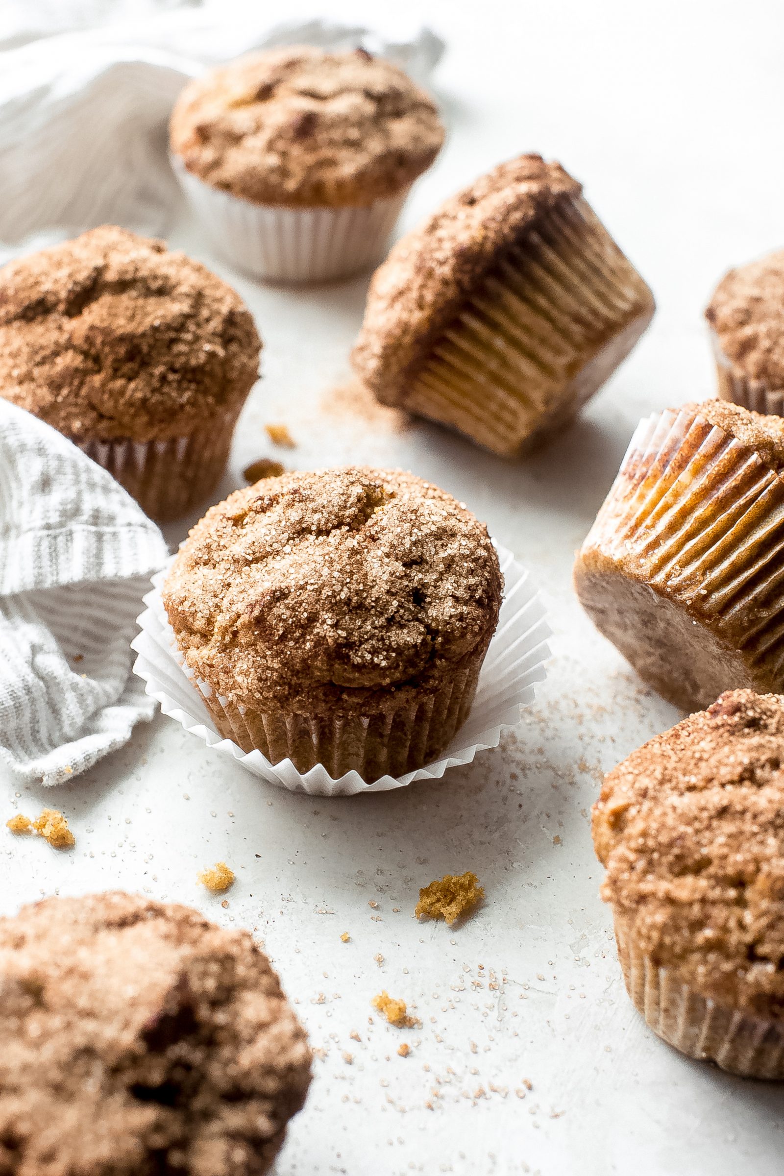 scattered muffin paper-lined pumpkin snickerdoodle muffins on a white surface