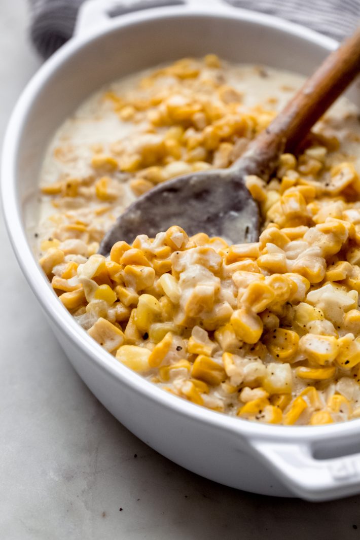 creamed corn in white dish with wooden spoon