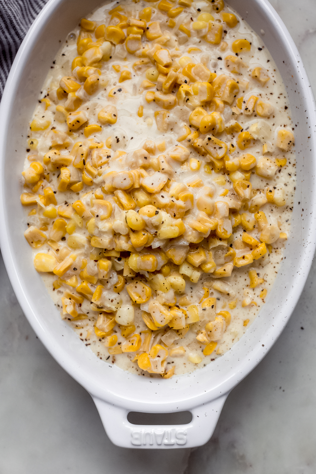 prepared creamed corn in white serving dish topped with crackers pepper