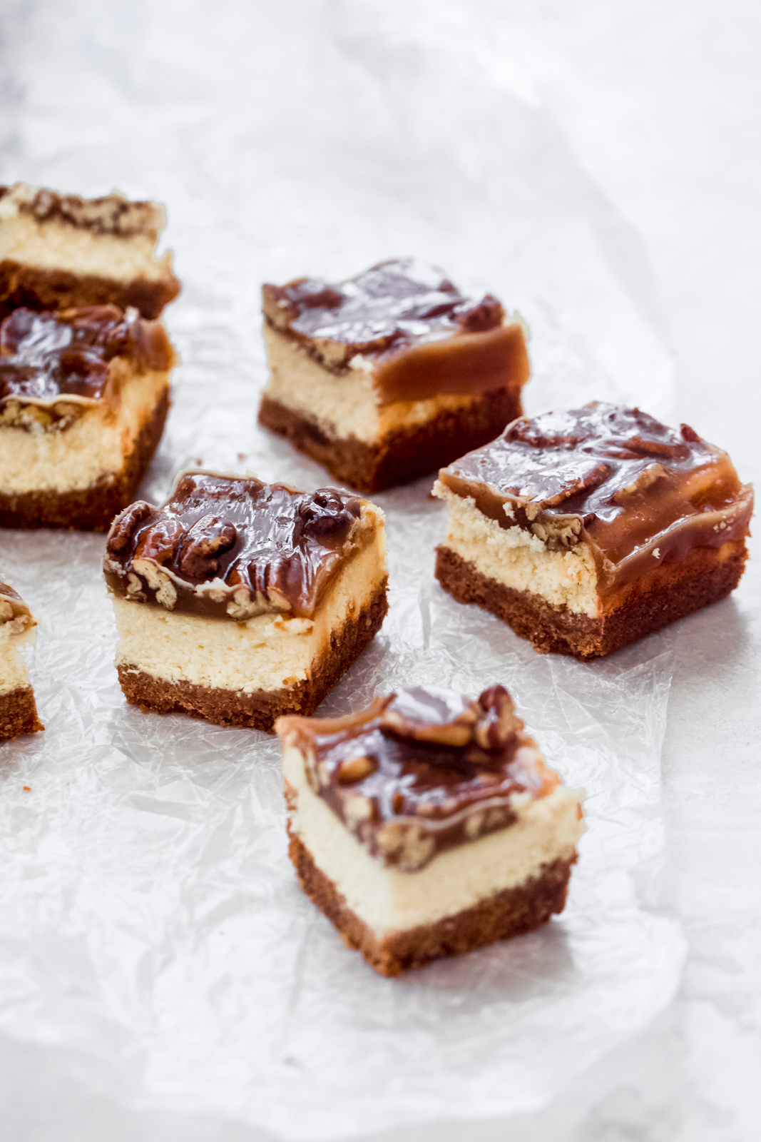 pieces of caramel pecan cheesecake bars on parchment paper on grey surface