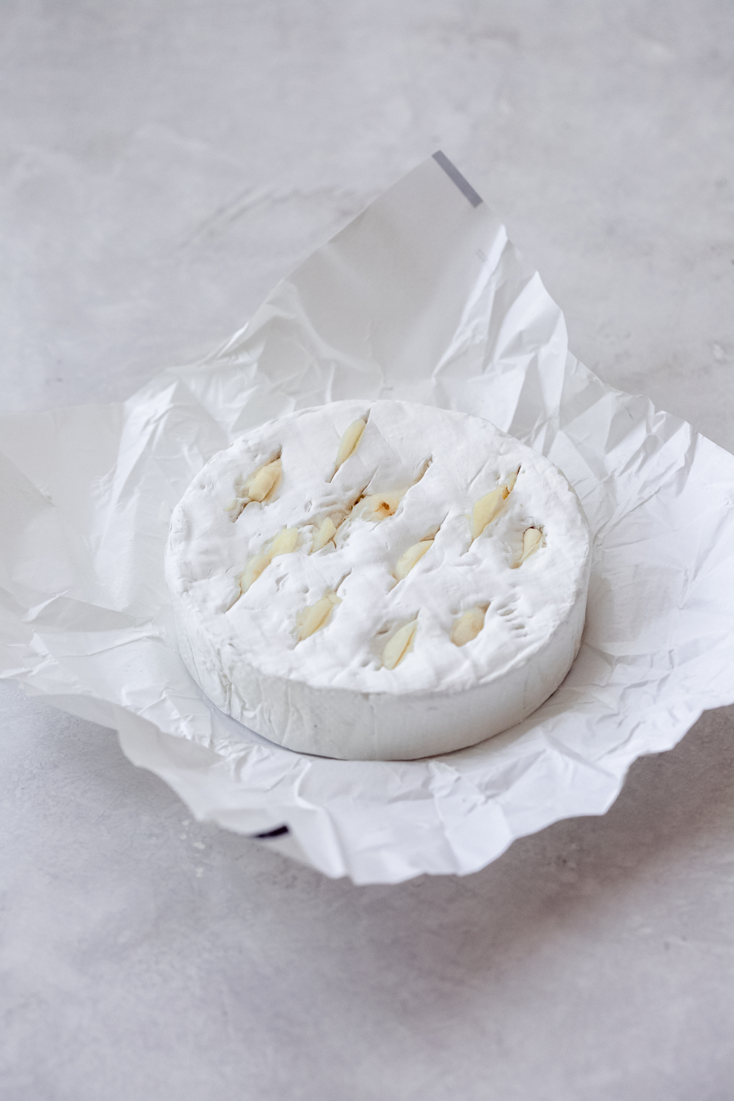 wheel of brie on wax paper with slits filled with garlic
