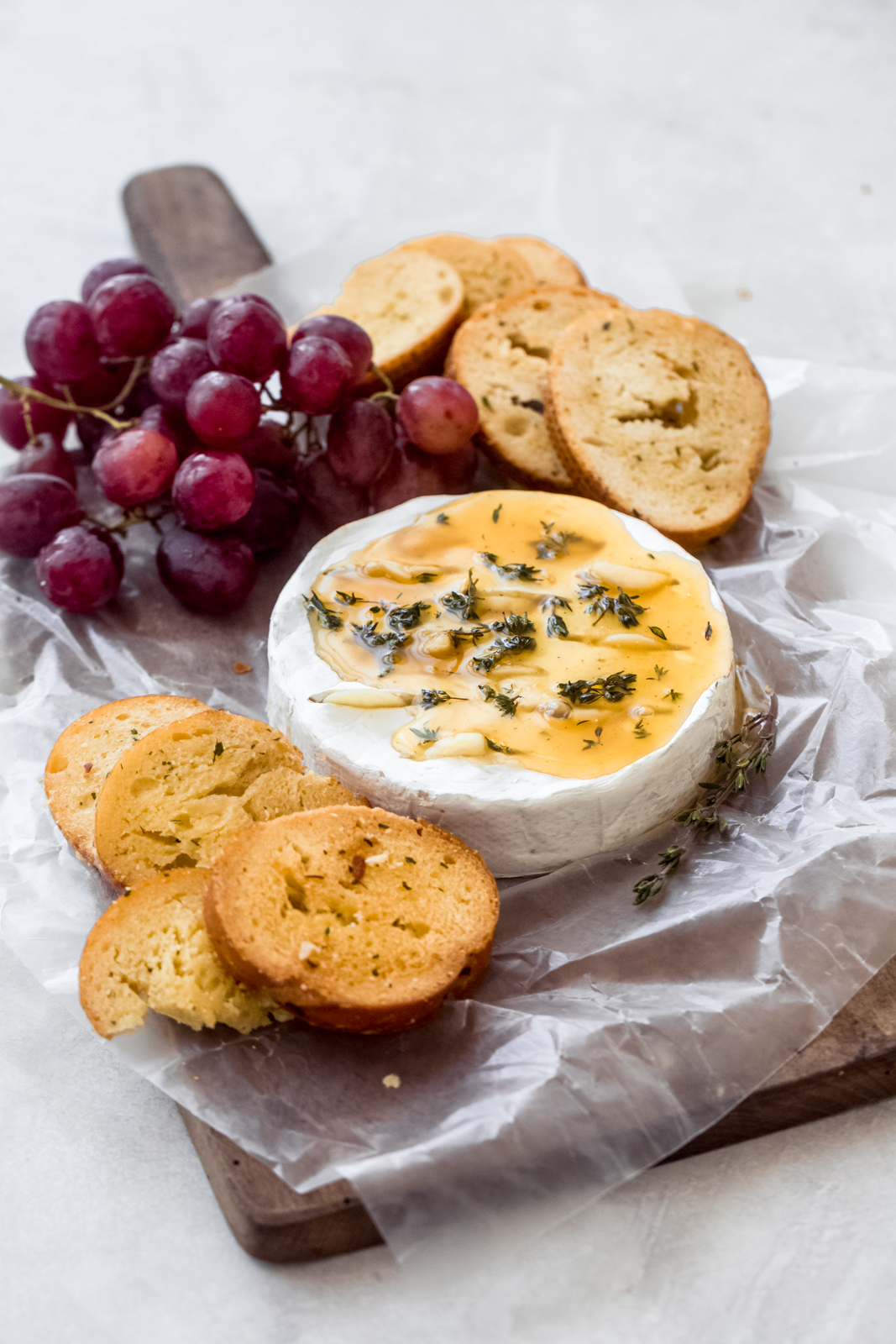 baked brie cheese on cutting board surrounded by grapes and garlic bread