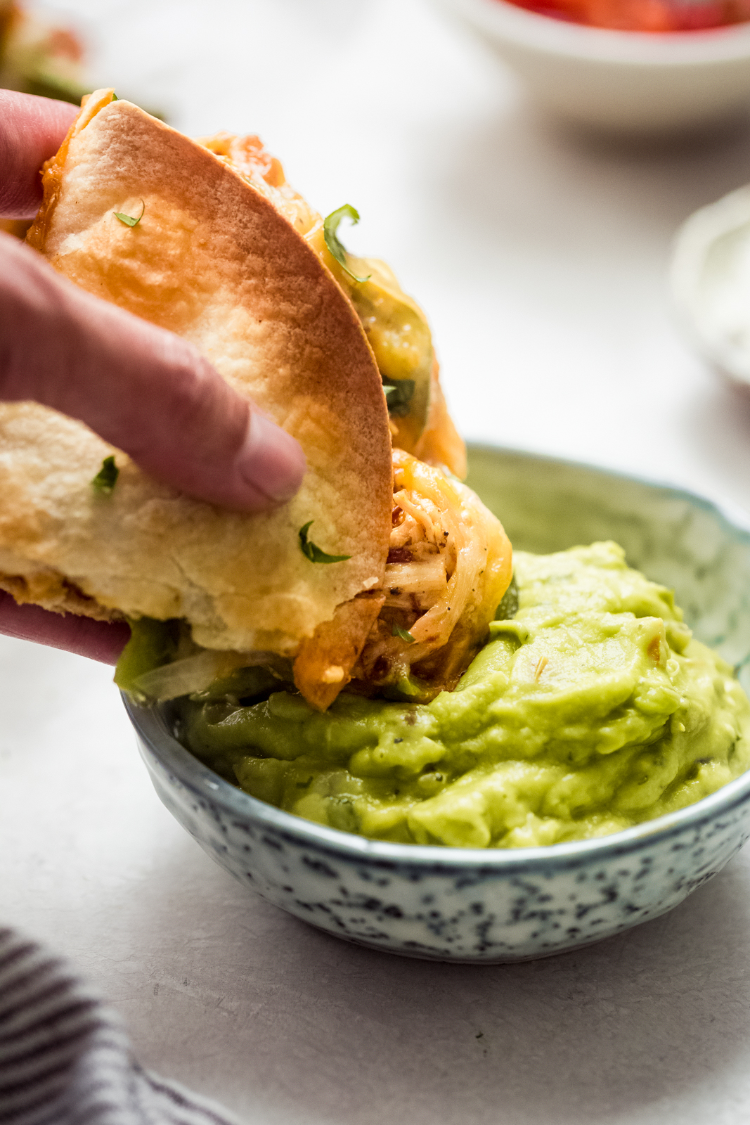 hand dipping baked chicken quesadillas in guacamole 