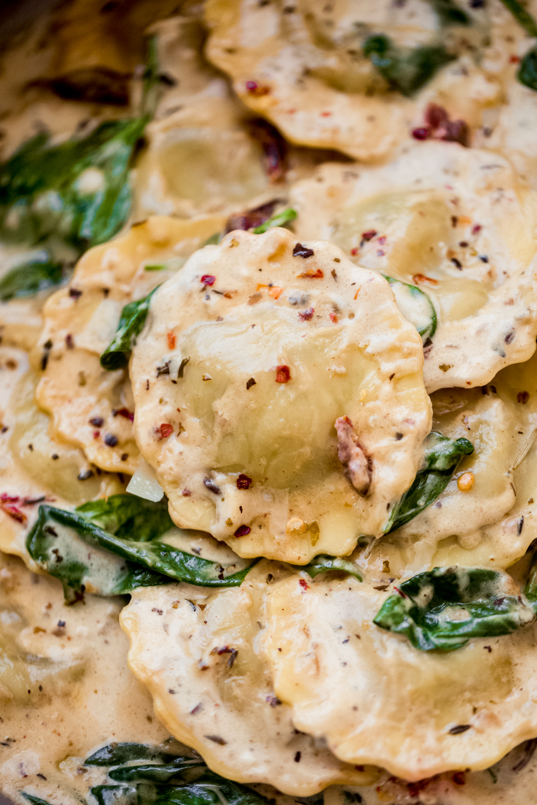 close up of ravioli in sauce with spinach topped with red pepper flakes