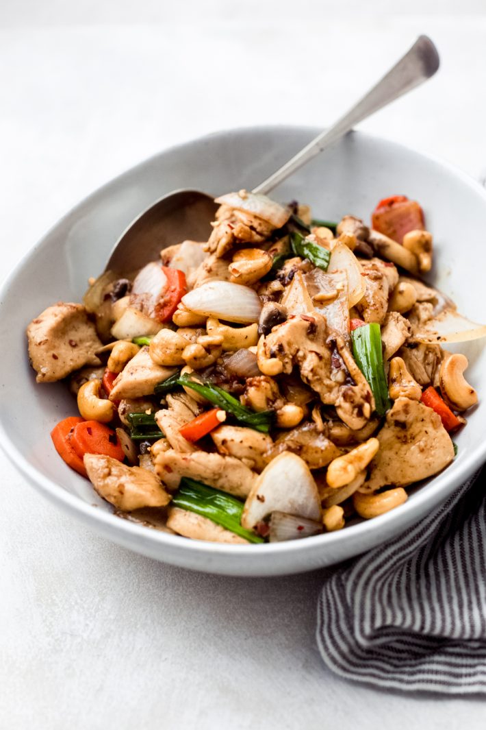 cashew chicken in white bowl with metal spoon