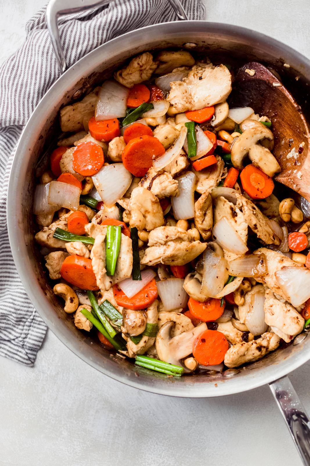 stainless steel pan with prepared cashew chicken with vegetables and wooden spoon