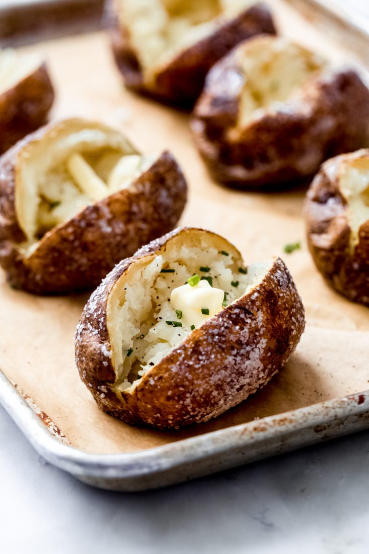 freshly baked potatoes on a sheet pan with butter and chives