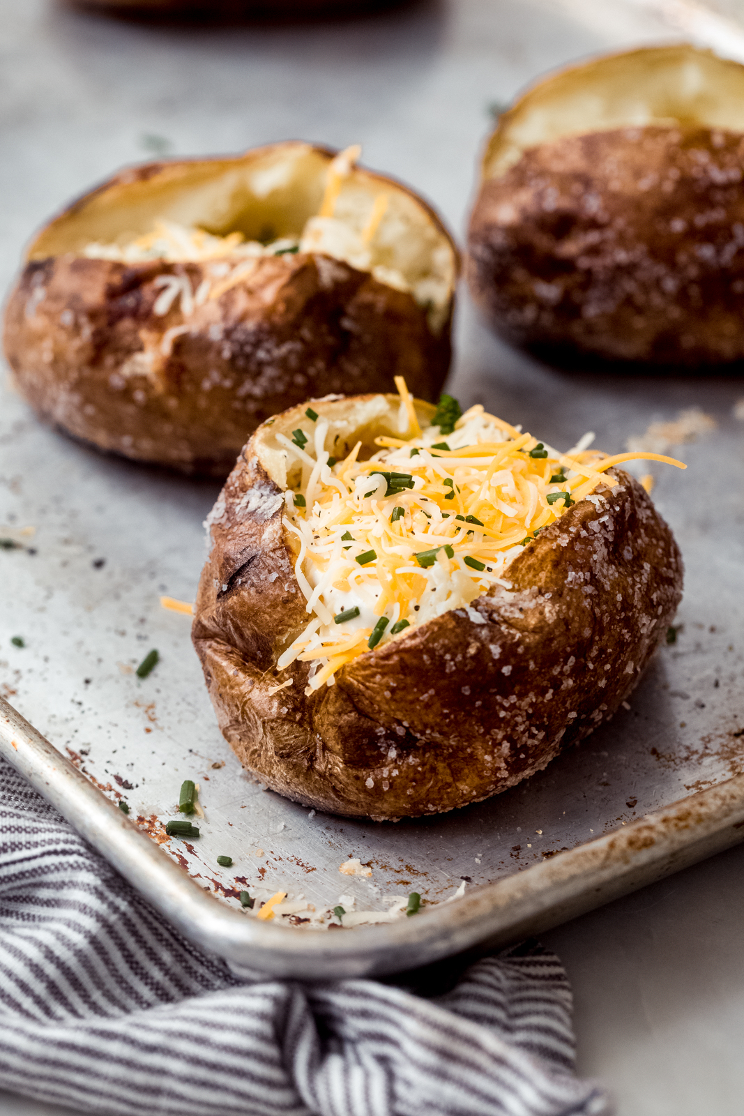 baked potato with shredded cheese and chives on sheet pan