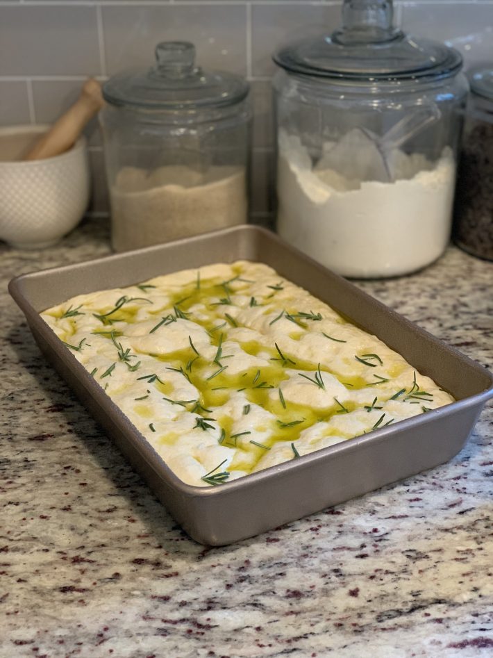 baking pan with focaccia dough with rosemary on granite counter