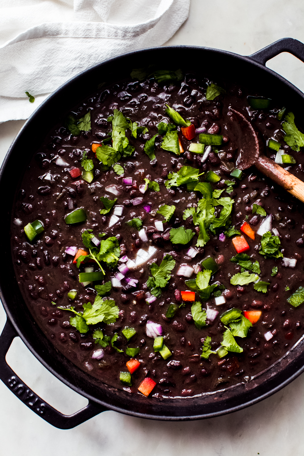 cuban black bean soup in cast iron pot topped with onions cilantro and peppers