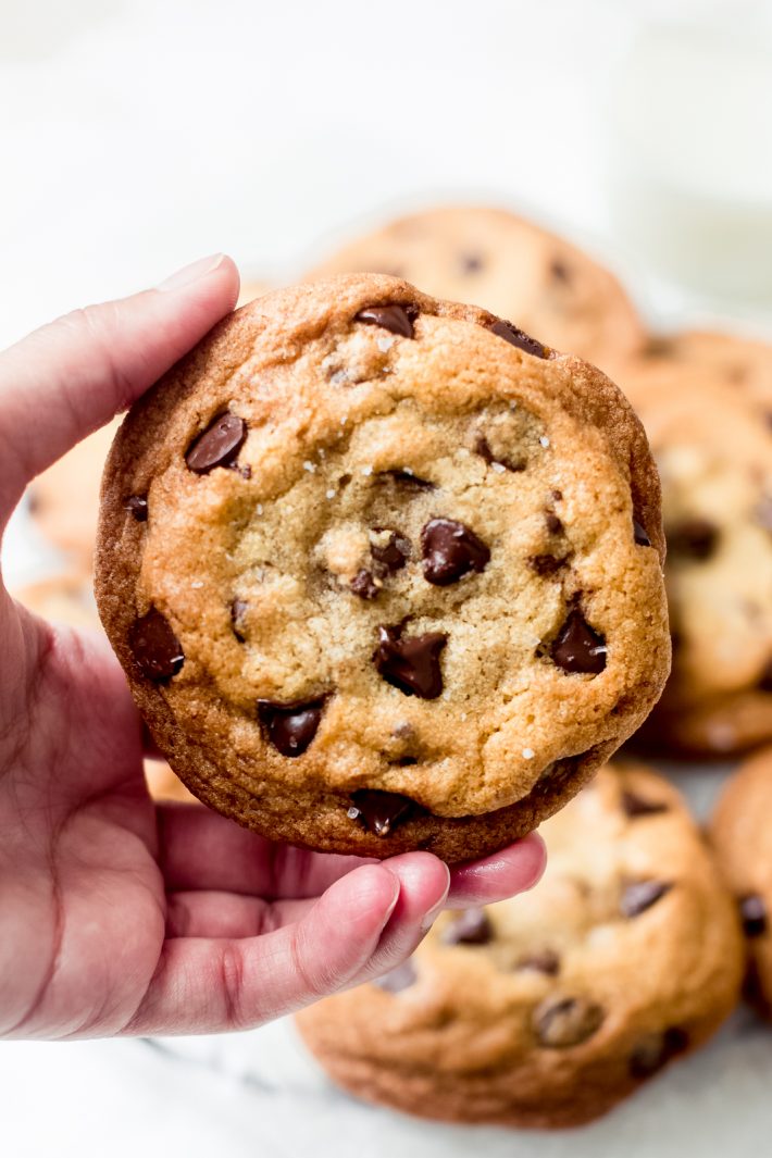a hand holding a chewy chocolate chip cookie 