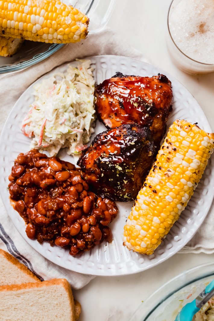 food scene with barbecue chicken, coleslaw, grilled corn, and baked beans