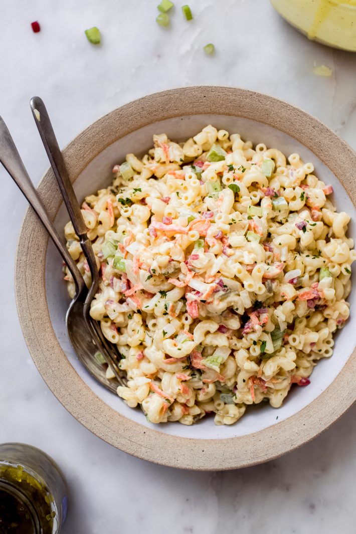 bowl of macaroni salad surrounded by sweet relish and prepared salad dressing