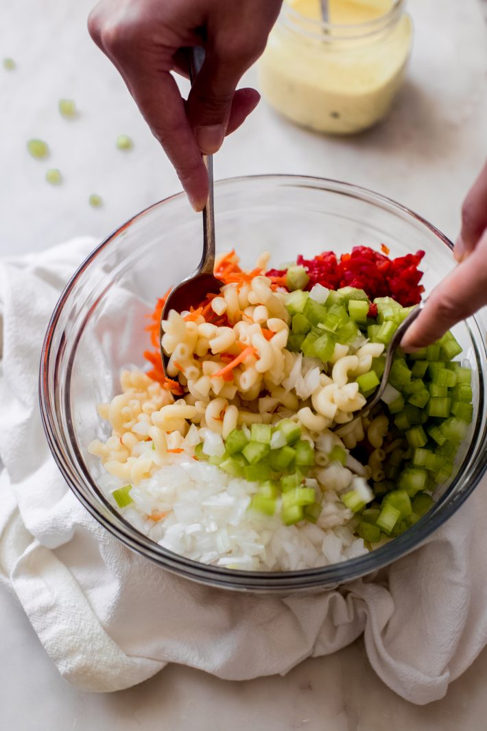 hands tossing cold pasta salad with vegetables