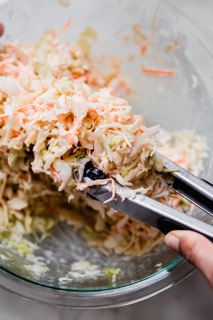coleslaw being lifted with a pair of tongs
