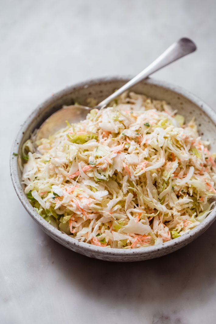side shot of prepared coleslaw recipe in grey speckled bowl with a spoon for serving