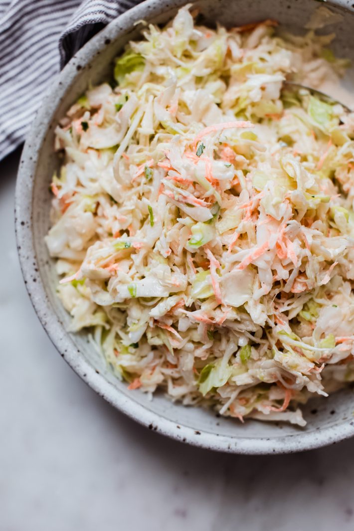prepared and dressed coleslaw in grey speckled bowl on white marble surface