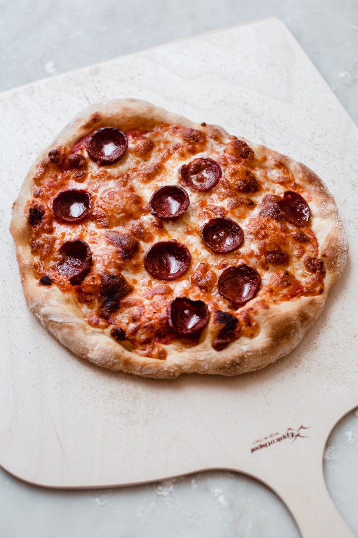 freshly baked no knead pizza dough topped with sauce, pepperoni, and melted cheese or pizza peel