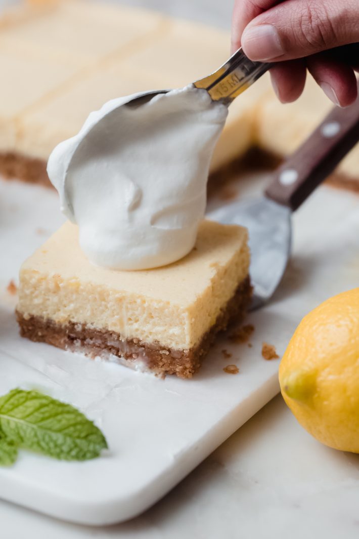 dollop of whipped cream dropping from tablespoon onto lemon bars