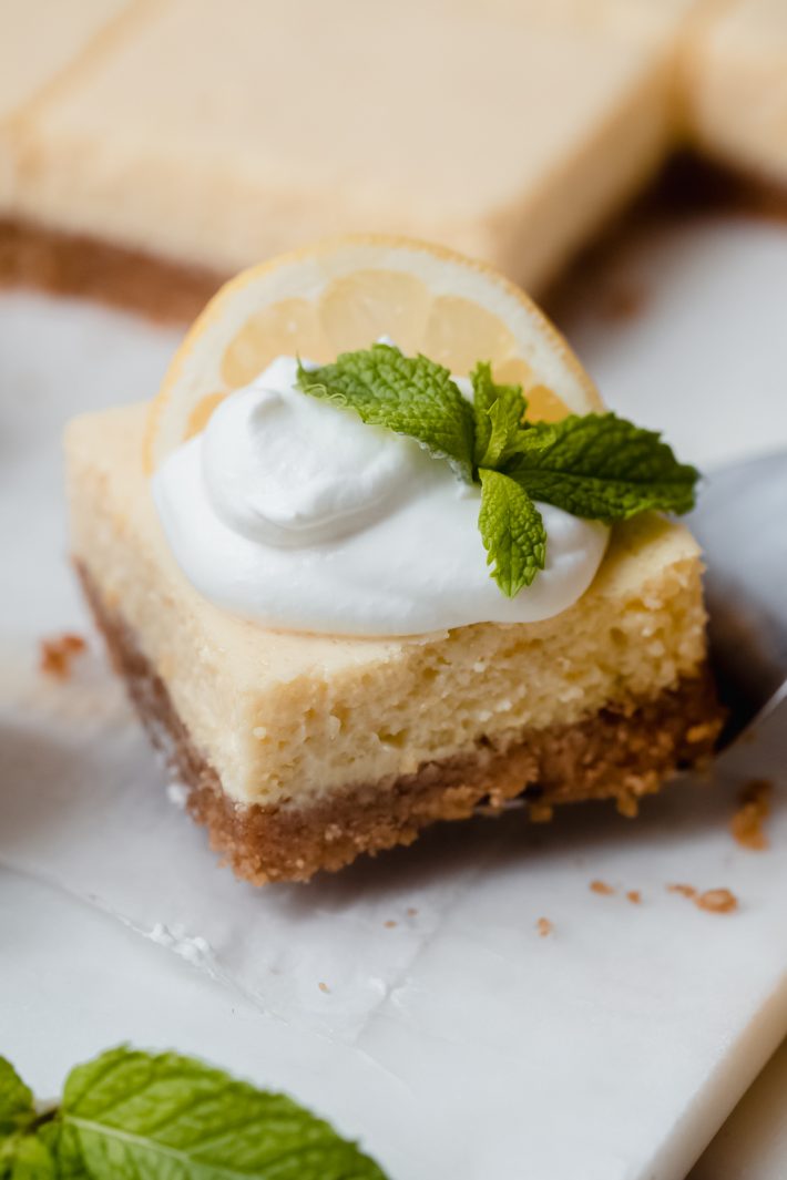close up of lemon square with whipped cream, mint, and lemon slice