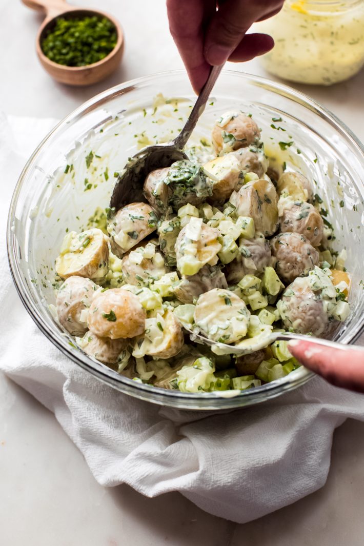 tossing sour cream chive potato salad with two spoons in glass bowl