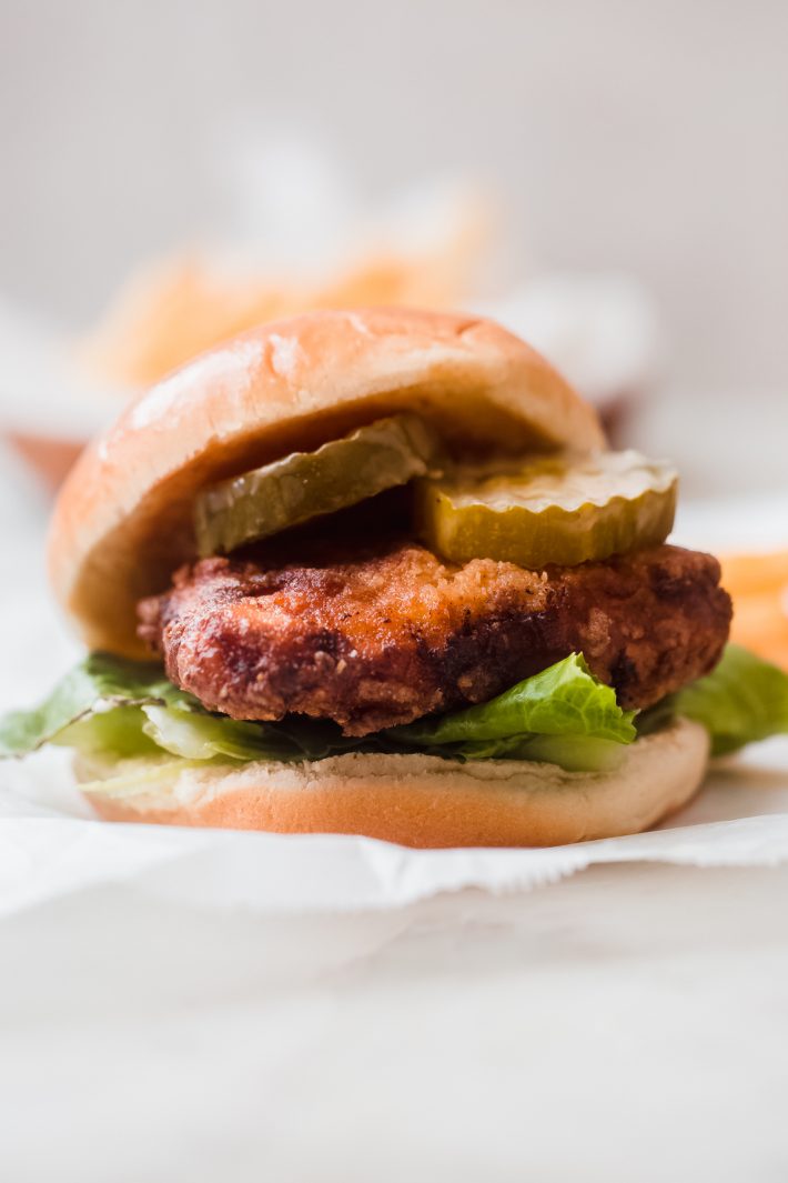 potato sandwich bun topped with fried chicken breast, pickles, romaine lettuce and sauce