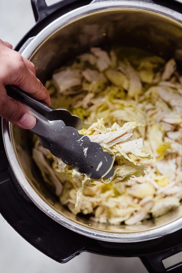 shredded chicken held up by tongs from the instant pot