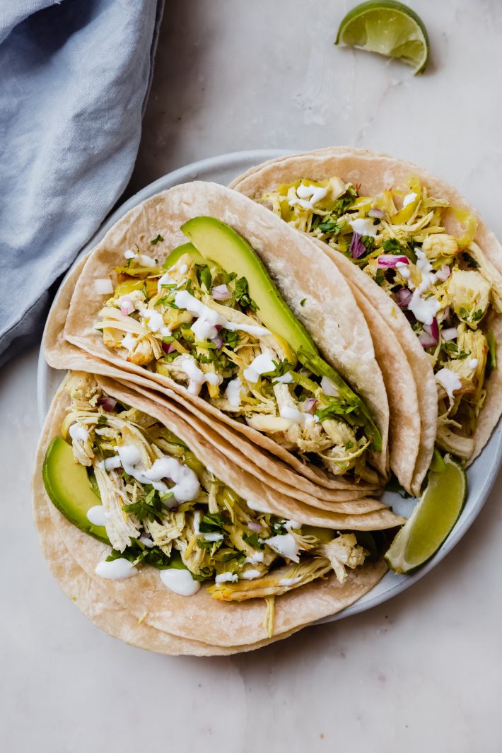 three pepperonicini chicken tacos on plate loaded with sliced avocados, minced onions, drizzled with sour cream