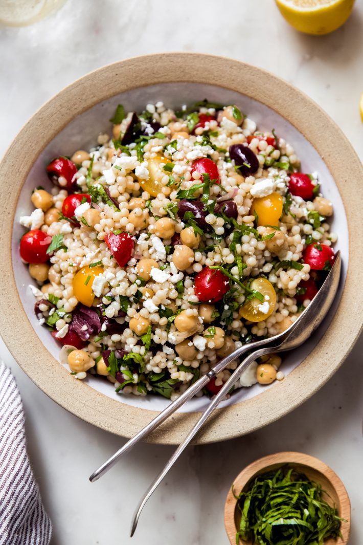 prepared Israeli couscous chickpea salad in rimmed bowl with spoon and fork